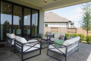 A modern patio area with sliding doors, featuring cushioned chairs and tables, enclosed by a neat lawn and a wooden fence, crafted by Texas builders.