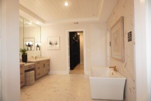 Modern bathroom with a freestanding bathtub, wooden vanity by Texas builders, wall-mounted mirror, and framed artworks on a white marble floor.
