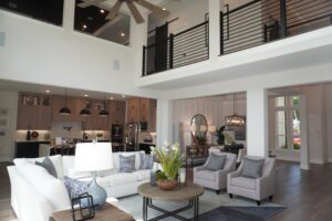 Spacious modern living room with high ceilings, exposed beams, and an open kitchen layout, featuring neutral-toned furniture and ample natural light, crafted by Texas builders.