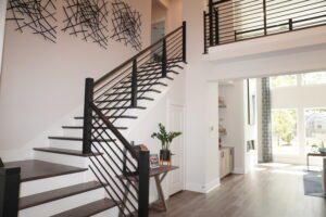 Modern interior with a dark wooden staircase, black metal railings, and a geometric wall decor in a bright, spacious room designed by Texas builders, featuring large windows.