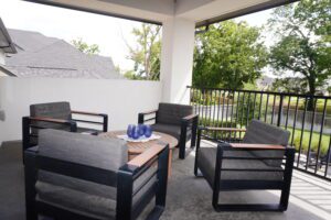 Modern outdoor patio setup with a dining table and chairs under a covered area, constructed by Texas builders, overlooking a suburban neighborhood.