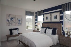 Modern bedroom with a white and navy color scheme, featuring striped patterns, abstract wall art, and a wooden headboard designed by Texas builders.