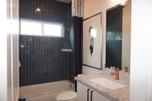 Modern bathroom with navy blue herringbone wallpaper, white fixtures, and a marble vanity crafted by Texas builders. A small frosted window lets in natural light.