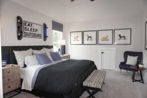 A modern bedroom with a black bed, skateboard-themed wall decor by Texas builders, three animal prints on the wall, and a blue armchair.