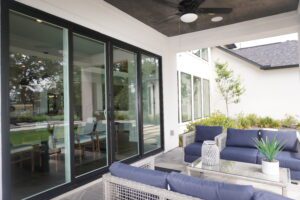 A modern patio area with wicker furniture and cushions, overlooking a garden through large sliding glass doors, crafted by Texas builders.