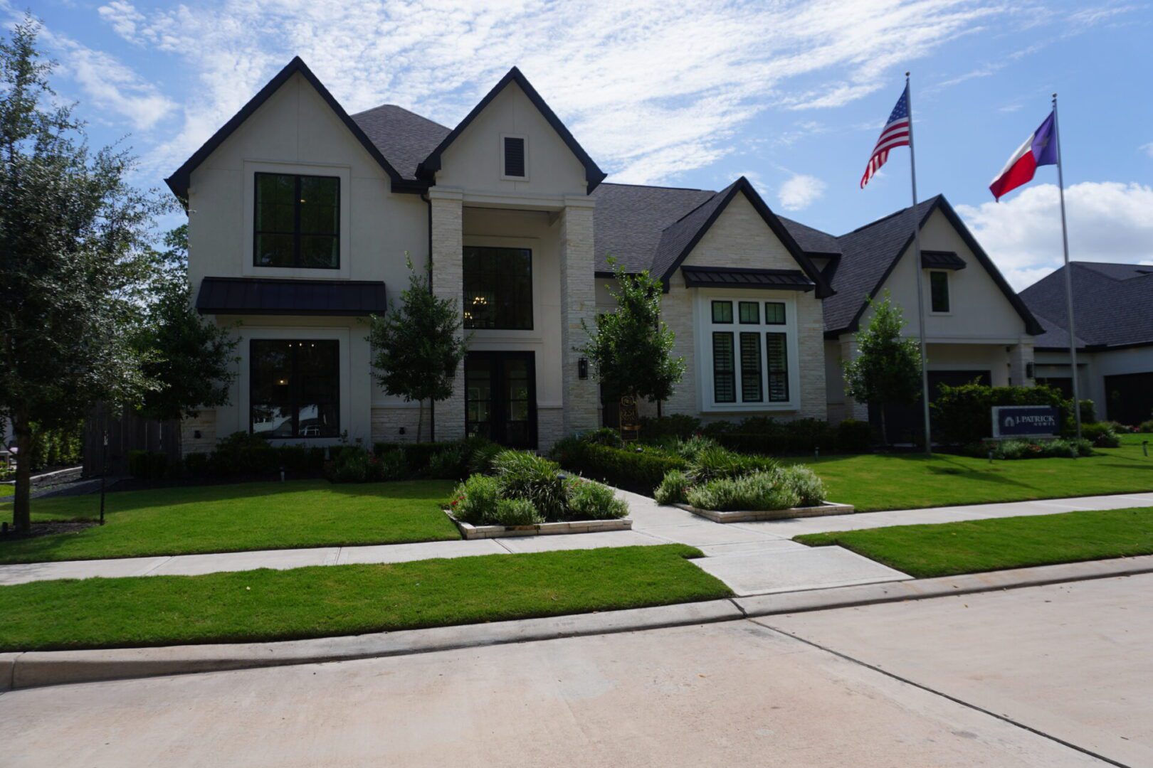 A large suburban house built by Texas builders with a well-maintained front lawn, featuring U.S. and Texas flags flying on a flagpole.