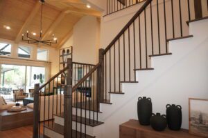 Interior of a modern home featuring a wooden staircase with black metal railings, constructed by Texas builders, leading to an upper floor, and decorated with large vases near the base.