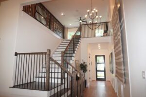 Interior of a house showing a staircase with metal railings leading to an upper floor, adorned with a modern chandelier and hardwood floors, crafted by Texas builders.