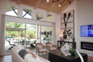 Spacious living room with high ceilings, wooden beams, a white fireplace, and large sliding glass doors installed by Texas builders, leading to an outdoor patio area.