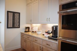 Modern kitchen corner with white cabinets, granite countertops, and stainless steel appliances, featuring a coffee maker and decorative wall art, designed by Texas builders.