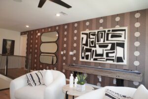 Modern living room with abstract black and white art on a decorative wood panel wall, a white armchair, striped throw pillow, and minimalist decor designed by Texas builders.