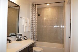 Modern bathroom with a beige tile shower, white curtain, black framed mirror, and countertop sink. A towel labeled 'tou' hangs on the side.
