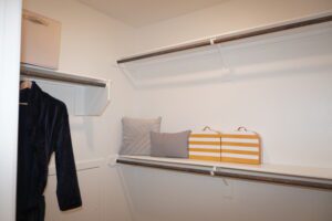 An empty closet with two hanging rods, one shelf with a storage box crafted by Texas builders, and a few clothes items including a jacket.