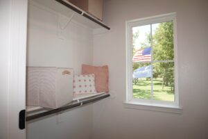 Interior view of a closet with shelves holding storage boxes and a pillow, beside a window displaying an American flag outdoors, constructed by Texas builders.