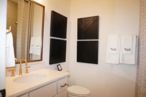 A modern bathroom interior designed by Texas builders, featuring a white sink, gold faucet, mirror, and decorative black panels on the wall, with neatly hung white towels labeled "toil.