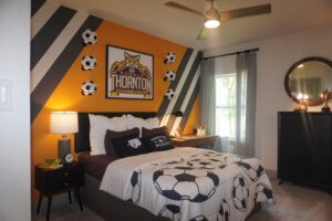 A soccer themed bedroom designed and constructed by Texas builders, featuring a cozy bed and a refreshing fan.