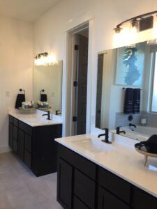 Modern bathroom interior crafted by Texas builders, featuring double vanity sinks, large mirrors, and black cabinets, with bright lighting and a neutral color palette.
