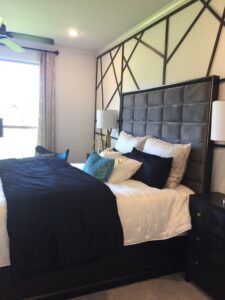 Modern bedroom designed by Texas builders, featuring a large geometric headboard, black and white bedding, dark wood furniture, and a green ceiling fan.