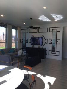 Modern living room with geometric wall art, black furniture, white floors, and large windows installed by Texas builders letting in natural light.