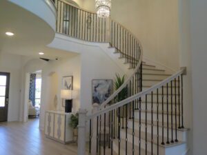 Elegant interior of a home featuring a curved staircase with a black wrought-iron railing, crafted by Texas builders, leading to an upper floor under a large chandelier.
