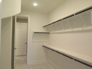 A spacious, empty closet constructed by Texas builders, with white walls and shelving along the sides, featuring a marble floor and a closed door at the end.