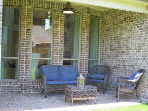 A cozy patio with brick walls, featuring a blue cushioned sofa, two wicker chairs, and a small table under a covered area constructed by Texas builders.