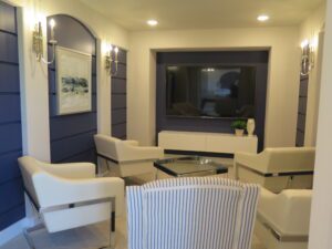 A cozy sitting area with two white chairs, a striped sofa, a glass coffee table, and wall-mounted lights, accompanied by a large mirror and artwork on a navy accent wall constructed by Texas builders.