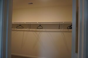 An empty closet with a shelf and rod holding three empty hangers, viewed through an open door, likely constructed by Texas builders.