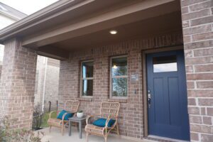 Front porch of a brick house with a blue door, two wicker chairs, and decorative plants crafted by Texas builders.