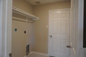 Interior of a small room with a white door, beige walls, and an empty closet built by Texas builders featuring a single white shelf and hanging rod.