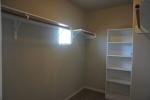Empty walk-in closet with beige walls featuring built-in shelves and hanging rods, lit by natural light from a small window, crafted by Texas builders.