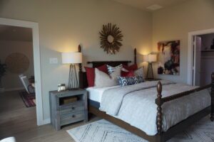 A stylish bedroom with a double bed, white and gray bedding, decorative pillows, flanked by bedside tables and lamps by Texas builders, and artistic wall decor.