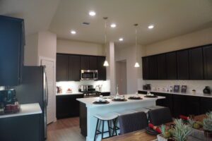 Modern kitchen with dark wood cabinets, white countertops, stainless steel appliances, a breakfast bar with stools, and pendant lighting by Texas builders.
