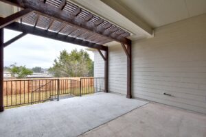 Covered patio area featuring a concrete floor, wooden slatted roof, and a metal railing overlooking a fenced backyard, constructed by Texas builders.