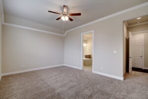 Empty room with beige carpet, gray walls, a ceiling fan, and doors installed by Texas builders leading to another room and a closet.