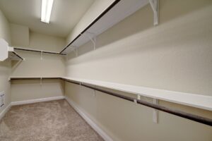 An empty walk-in closet constructed by Texas builders, featuring beige walls, multiple shelves, and a carpeted floor in a residential home.