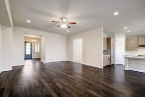 Empty living room and kitchen area with hardwood floors, white walls, and contemporary fixtures in a new home by Texas builders.