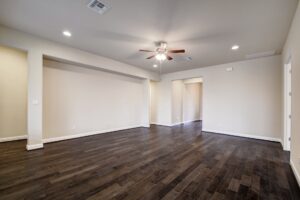 Empty living room with dark hardwood floors, white walls, and a ceiling fan. Two open doorways are visible, crafted by Texas builders.