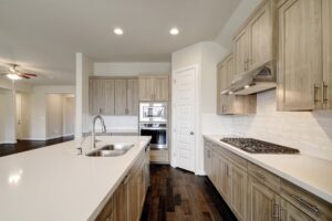 Modern kitchen interior with wooden cabinets, white countertops, stainless steel appliances, and dark hardwood floors constructed by Texas builders.