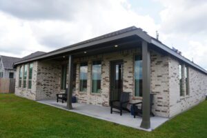 Brick house with covered patio and chairs.